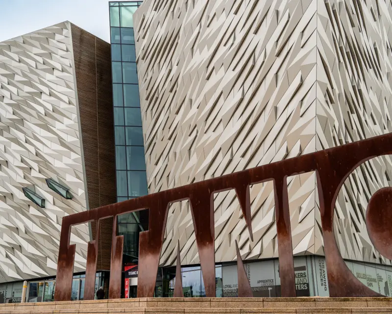 The striking exterior of the Titanic Belfast building with a large, rust-colored installation in front.