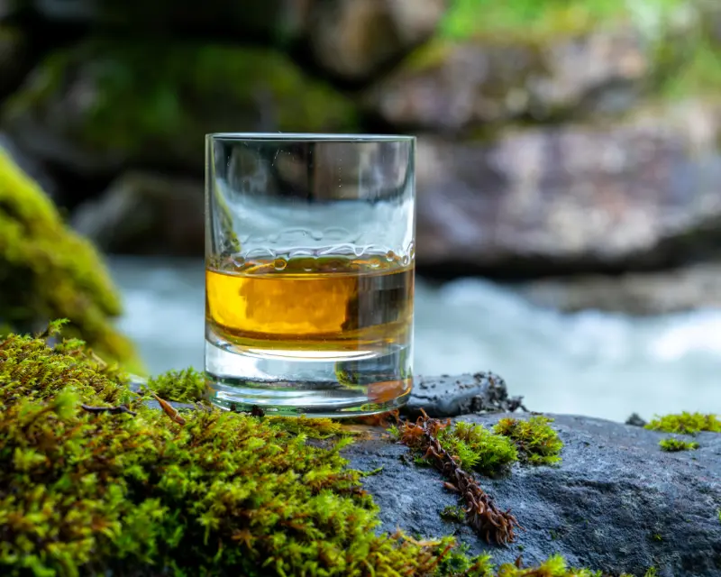 Glass of whisky on a rock by a fast flowing river