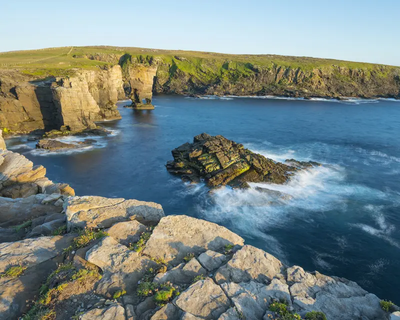 A scenic coastal landscape with rocky cliffs and calm blue waters, under clear skies, ideal for small group tours.