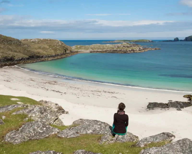 a woman sitting on a rock overlooking a beautiful beach