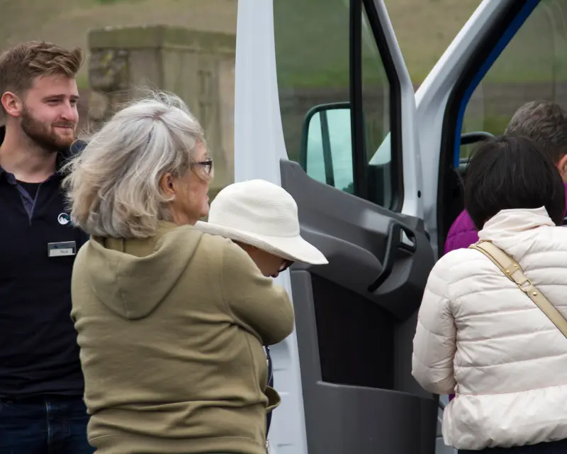 Tour group interacting by a van, with a guide and travelers preparing for a small group excursion in the UK.