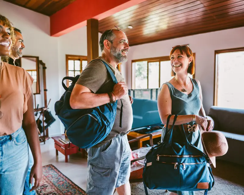 Three women smiling and chatting at a doorway, one welcoming the others, showcasing friendly connections and exploration.