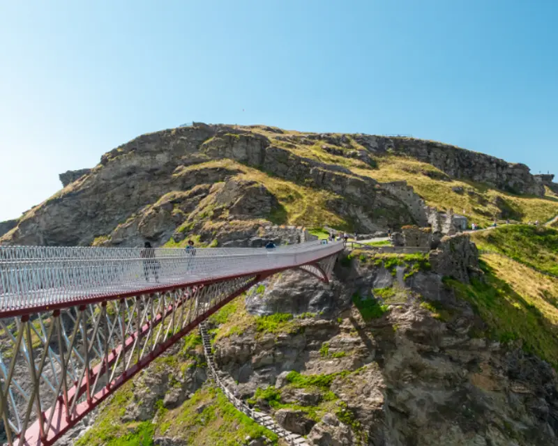 Suspension bridge connecting rocky terrain, surrounded by green hills under a clear blue sky, perfect for adventurous tours.
