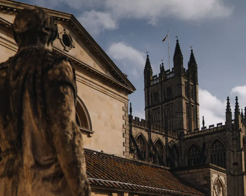 A close-up of a historic statue with a grand Gothic church tower in the background under a partly cloudy sky.