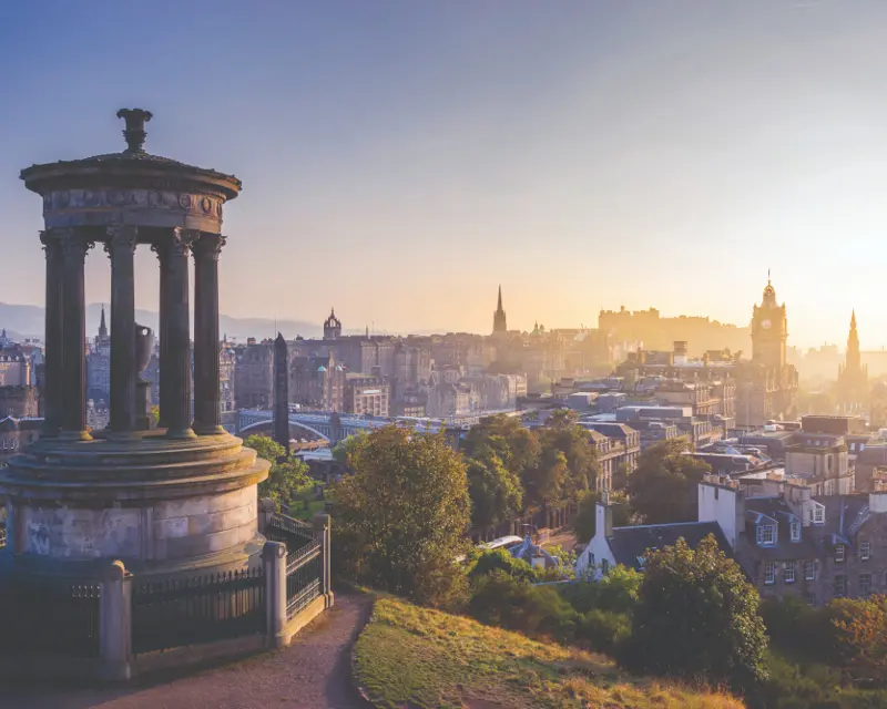 Sunrise over Edinburgh, featuring a scenic view from Calton Hill with historic architecture and lush greenery.