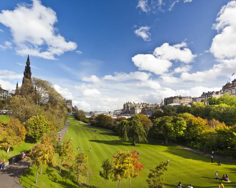 A scenic park scene in the UK with lush greenery, trees, and people enjoying the outdoors under a bright blue sky.
