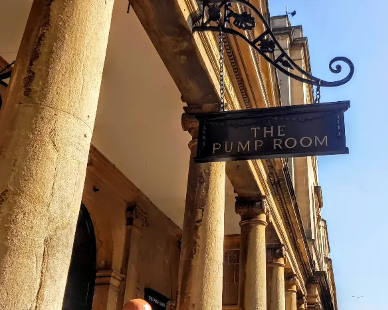 Sign for "The Pump Room" near classic columns, representing historic architecture in Bath, UK.