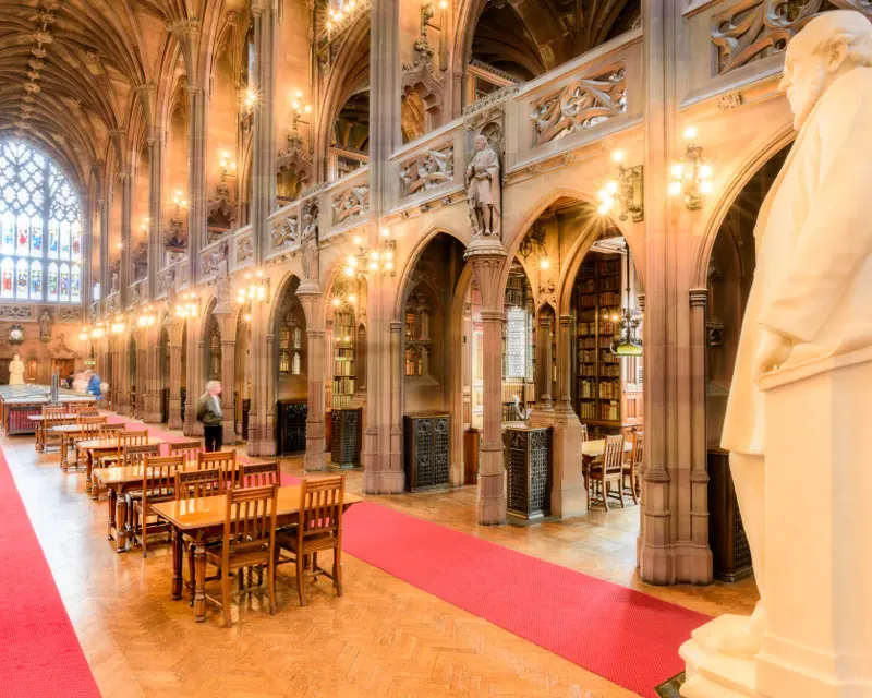A grand, historic library with wooden tables, arched ceilings, warm lighting, and a prominent statue, inviting exploration.