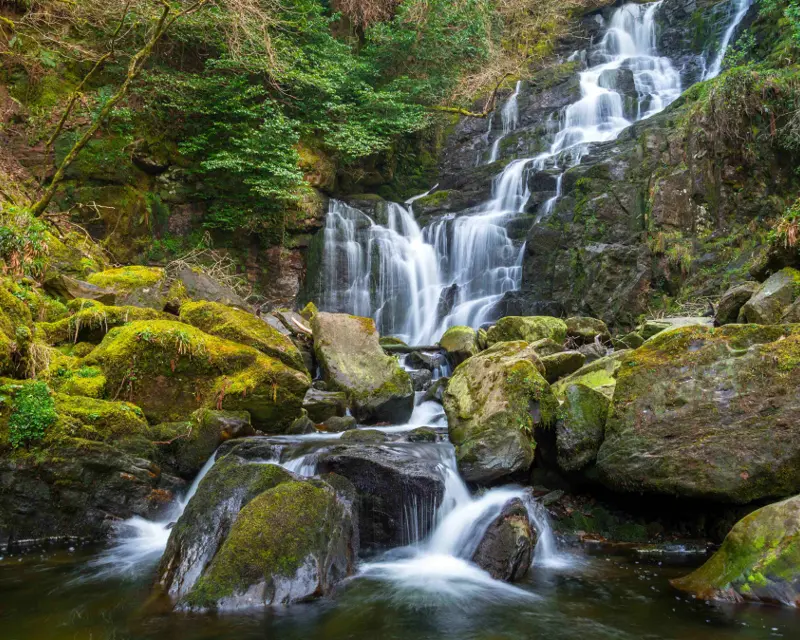 A serene waterfall cascades over moss-covered rocks, surrounded by lush greenery, showcasing the beauty of nature in the UK.