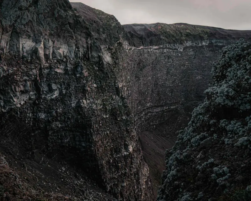 Dramatic view of a rugged volcanic crater, showcasing steep rocky walls and sparse greenery in the foreground.
