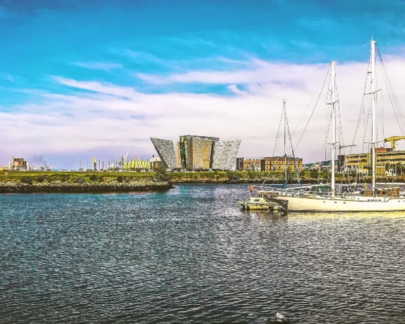 A scenic view of Belfast's waterfront, featuring the iconic Titanic Belfast building and sailboats on the water.