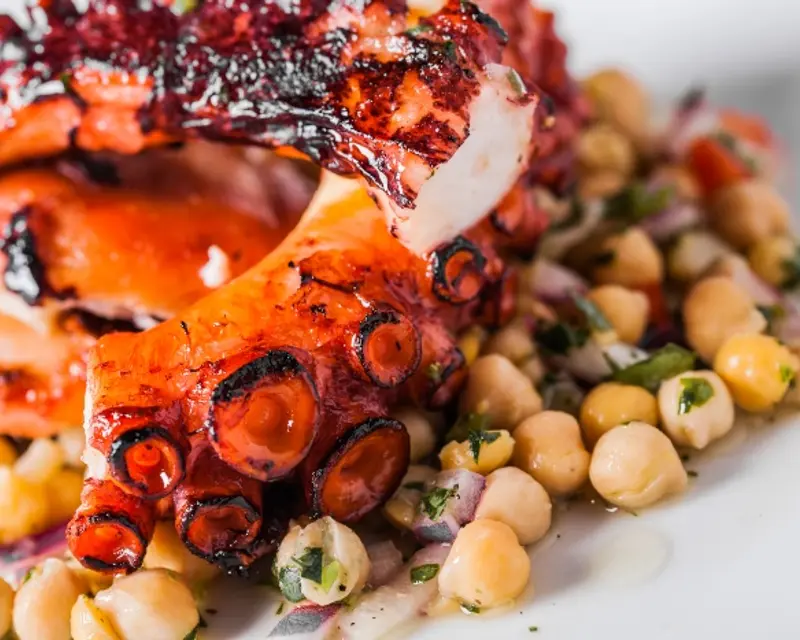 Grilled octopus served on a bed of chickpeas and garnished with herbs, showcasing a vibrant and appetizing dish.