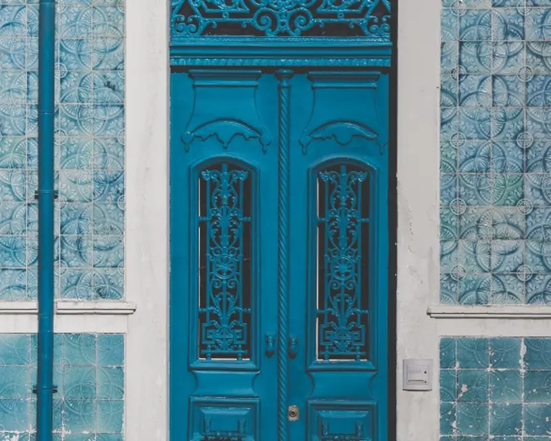 A vibrant blue door with intricate designs, framed by patterned blue tiles on the wall.