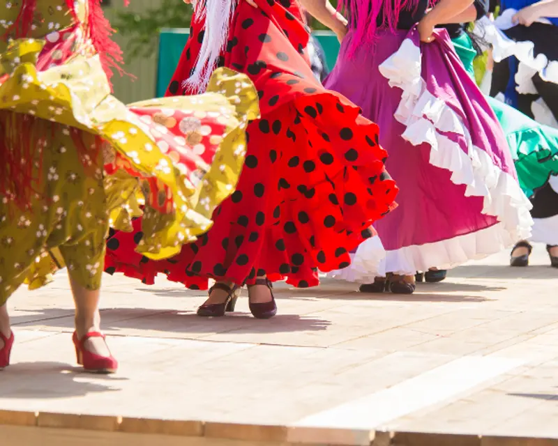 Colorful dresses swirl in motion, showcasing traditional dance on a sunny day, capturing vibrant cultural celebration.