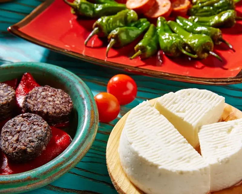 An array of vibrant dishes featuring cheese, black pudding, cherry tomatoes, and green peppers on colorful plates.