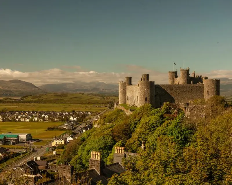 Historic castle perched on a hill, overlooking a scenic village and lush valleys under a clear blue sky.