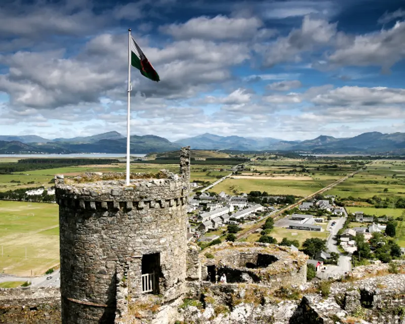 A panoramic view from a historic stone tower with a flag, overlooking lush valleys and distant mountains in the UK.