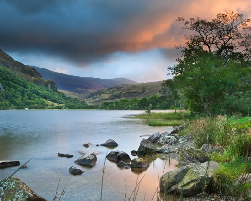 A serene lake surrounded by lush hills and dramatic skies, capturing the beauty of the UK's natural landscapes.