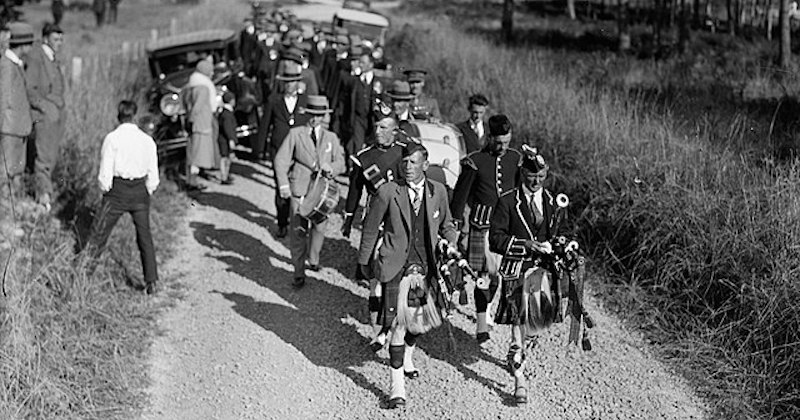 a black and white photo of a procession of men wearing traditional tartan kilts