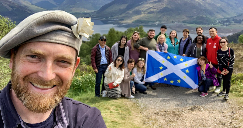 small group tour and tour guide posing for a photo on a mountain with a scottish flag