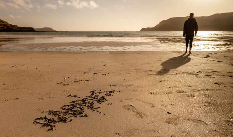 a man on a wide and empty beach in Ireland with 'Rabbie's' written in the sand