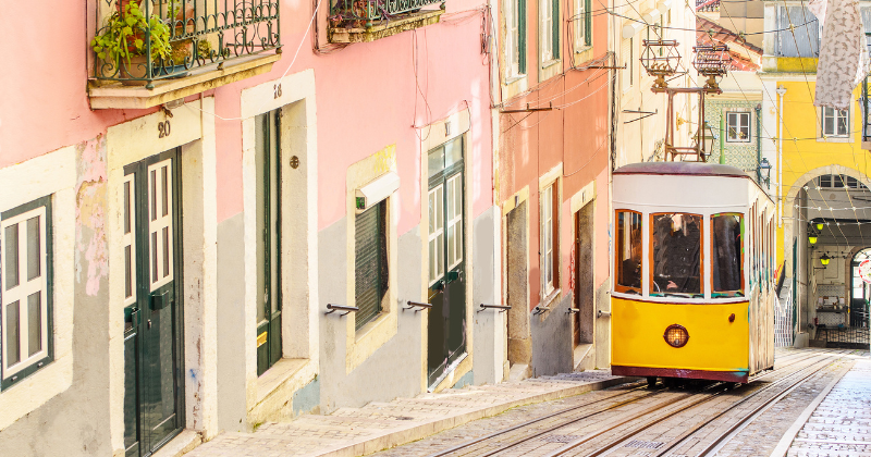 a yellow tram passing colourful houses on a hill in Lisbon