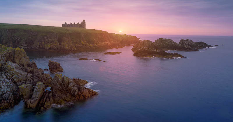 A view of Scotland's Slains Castle perching on a cliff at sunset