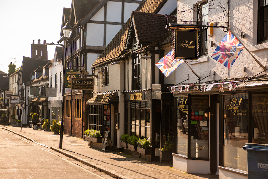 a row of older buildings on a high street, including a bnb, with vintage signs hanging from their second floor