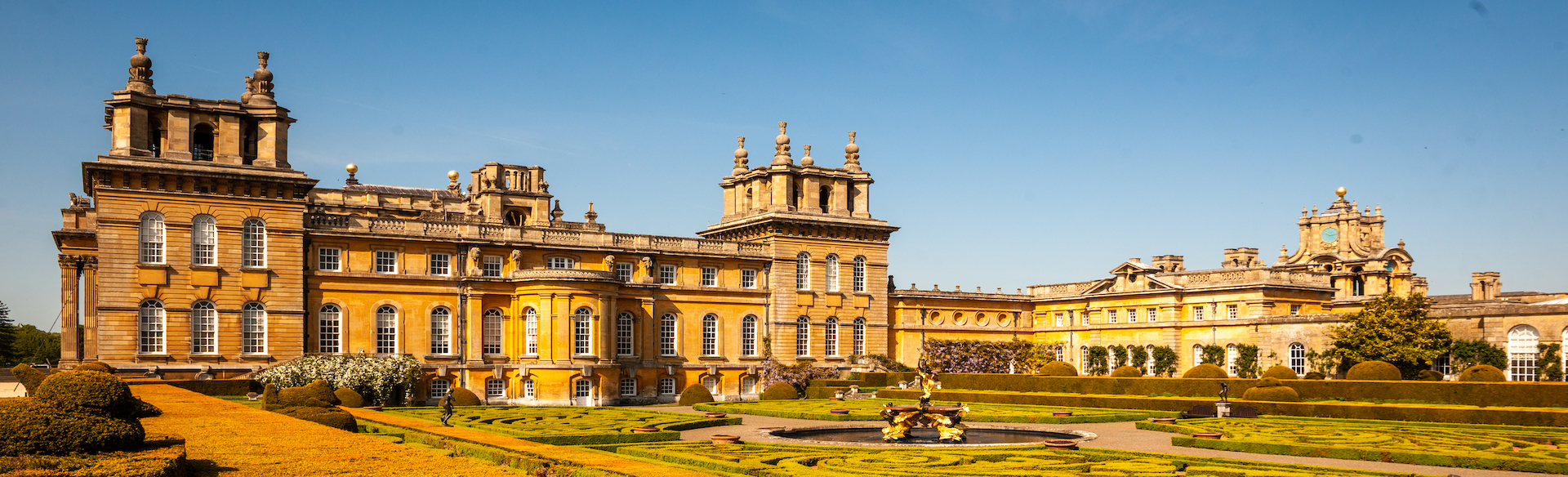 the grand sandstone structure of Blenheim Palace and it's luscious gardens under a blue sky