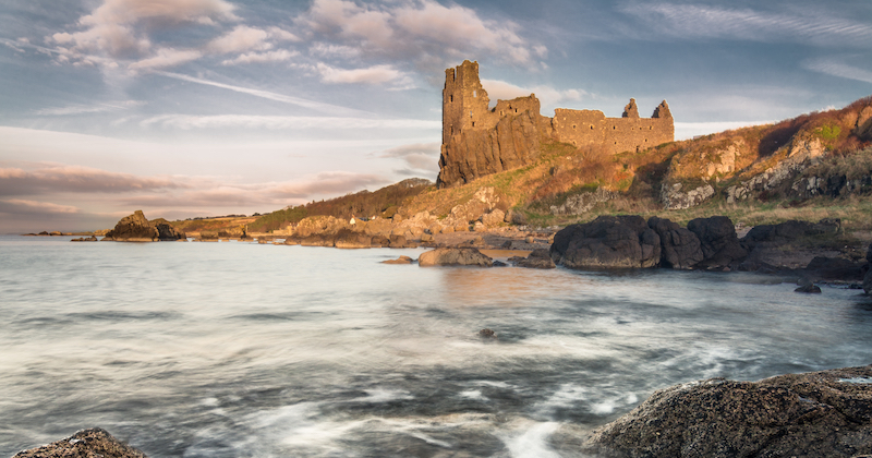 the ruins of Dunure castle on a coastal cliff can be visited via direct flights to Scotland from USA
