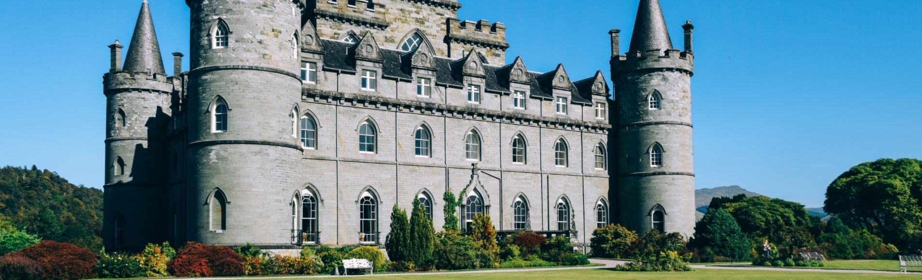 an impressive Scottish castle under a blue sky and surrounded by autumnal trees down a long stoned driveway