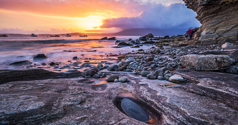 The dramatic and rocky coastline of the Isle of Skye under the purple light of a sunset