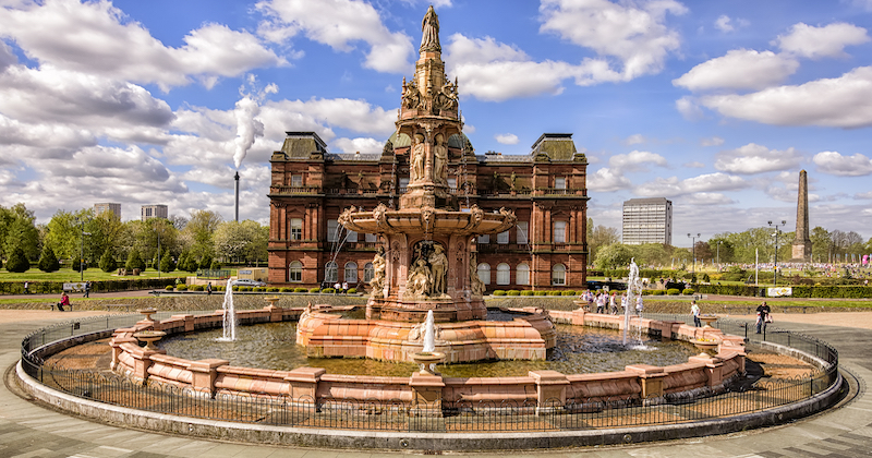 The tall and highly decorative Doulton Fountain in the centre of Glasgow under a blue sky with white clouds.