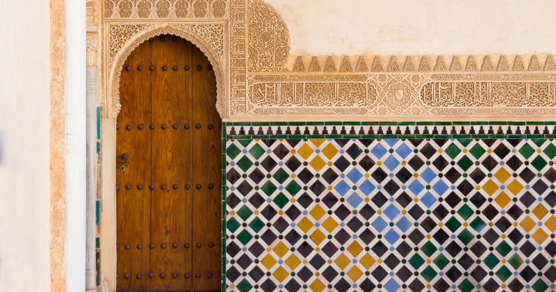 the intricate blue, green and yellow mosaics and a carved wooden door of the Alhambra Palace in Spain