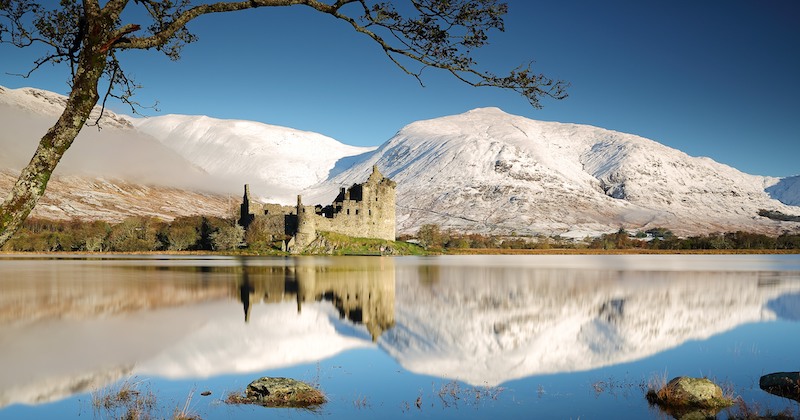 the ruins of Kilchurn castle in winter with snowcapped mountains in the background