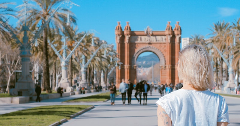 a solo traveller admiring Spanish architecture on a palm tree lined road under a clear blue sky