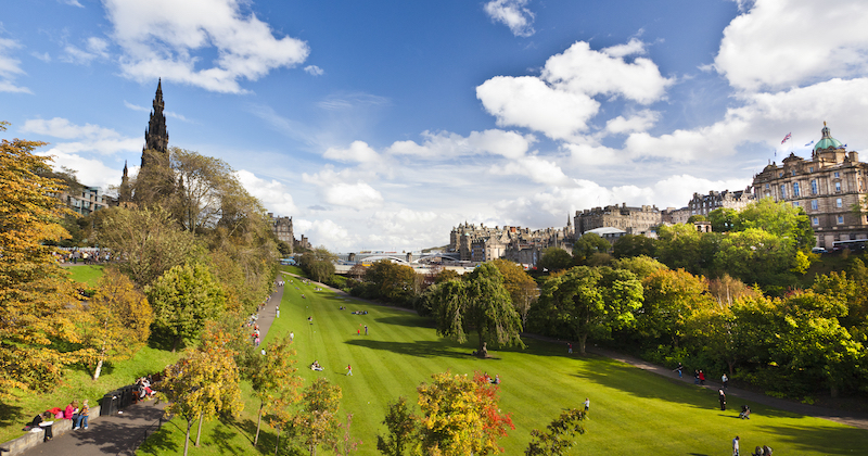 Underneath a clear blue sky people are relaxing on the green grass of Princes Street Gardens in Edinburgh